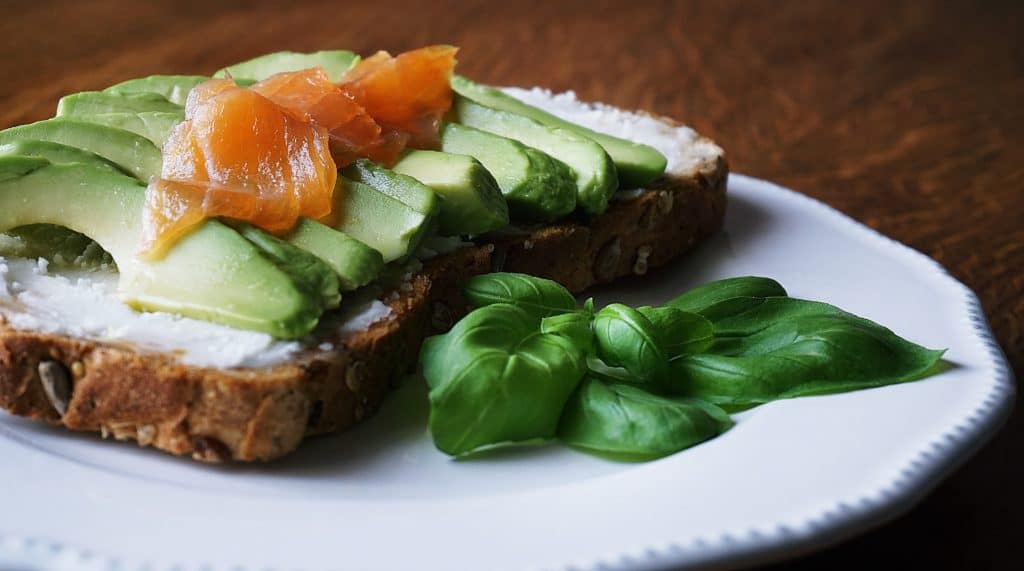 Slice of bread with avocado, smoked salmon and fresh basil leaves